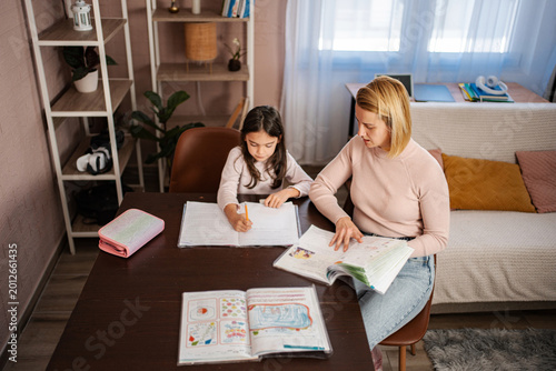 Foto Mother helping daughter with homework during homeschooling lessons