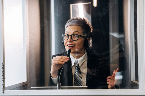 Tableau sur toile Female interpreter wearing headset speaks into microphone inside soundproof boot