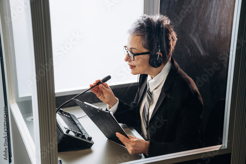 Photos Female interpreter wearing headset speaks into microphone while seated in soundp
