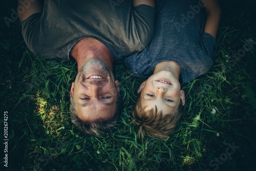 Father and son relaxing on grass in a sunlit park