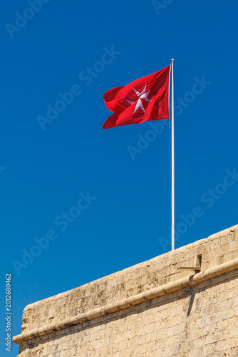 Konstfotografi Red Maltese cross flag waving on a historic fortress wall