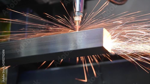 Slow motion video of fiber laser cutting machine engraving and slicing a metal square tube with intense sparks.