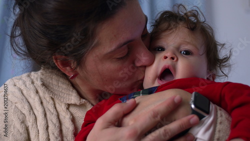 фотографія Mother kissing baby close up, infant reacts with wide-eyed surprise and open mou
