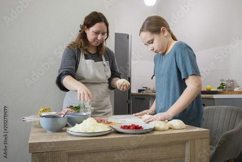 Lifestyle portrait of daughter and mother cooking italian pizza together in cozy domestic kitchen. Family preparing food at home