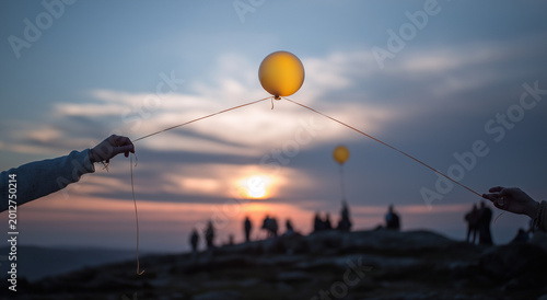 a hand holding a string with an exploding balloon, floating in the sky at sunset