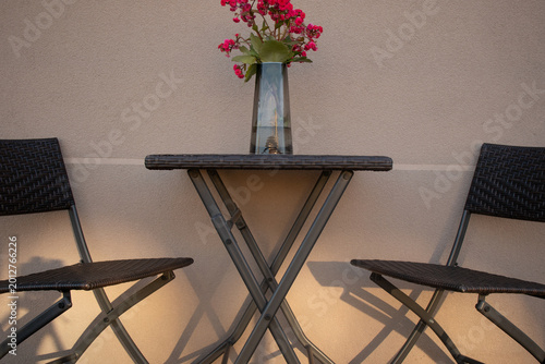 Outdoor patio furniture set with pink flowers in a vase on a balcony at sunset