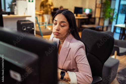 Tired businesswoman closing eyes at desk in modern office
