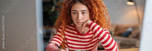 Teen girl looking thoughtful while using computer at home desk