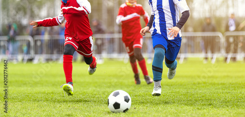 Dynamic Action Shot of Youth Soccer Players Sprinting for the Ball During Outdoor Tournament Match - Junior Athletes in Red and Blue Uniforms Competing on Pitch