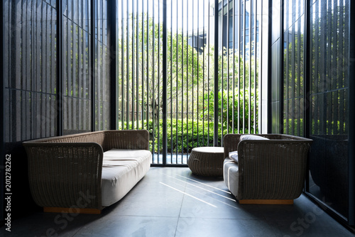 Schilderij op canvas Modern wicker sofa set in a serene courtyard with lush greenery and vertical gla