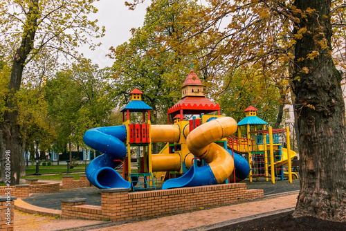 Fotografija Vibrant children's playground with large blue and yellow spiral tube slide, castle towers, and play elements in green spring park