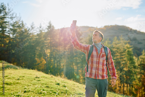 Canvastavla Man actively holding a smartphone up, searching for a signal while hiking in a s