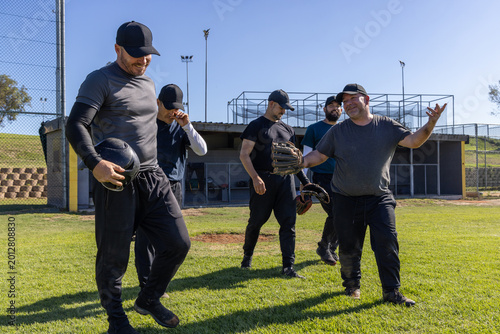 Billede på lærred Diverse male teammates walking across grassy baseball field near dugout, holding