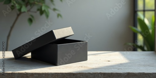 A partially opened black gift box rests on a weathered wooden surface, bathed in soft sunlight filtering through a nearby window, creating a serene and minimalist scene.
