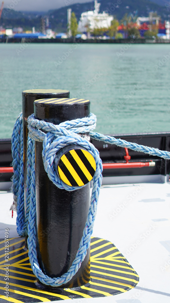 Fototapeta premium Blue mooring rope tied around a black and yellow striped bollard on a ship deck