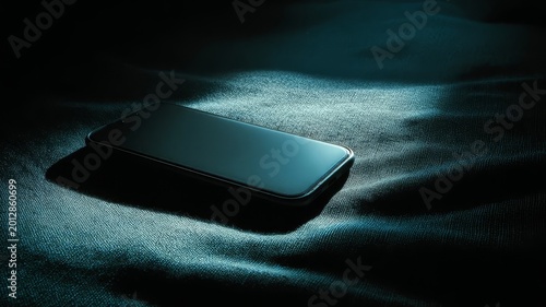 Dark phone rests on textured fabric under cool blue light
