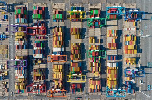 Aerial view of a busy port container yard with stacked shipping containers and gantry cranes in operation
