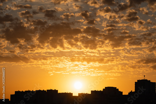 Golden sunset with textured clouds over the silhouette of a residential city district in Tallinn, Estonia, providing a peaceful urban landscape.