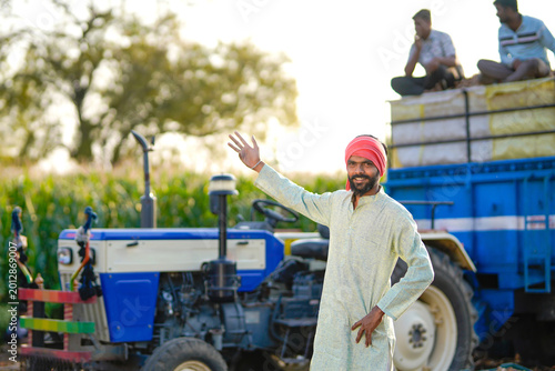 Canvas Print young indian farmer using smartphone standing with tractor at agricultural field