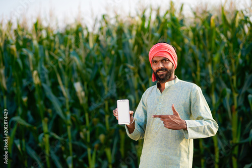young indian farmer showing smartphone screen standing at cornfield
