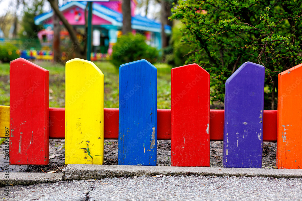 Fototapeta premium Bright multicolored wooden picket fence on a playground in a park, selective focus.
