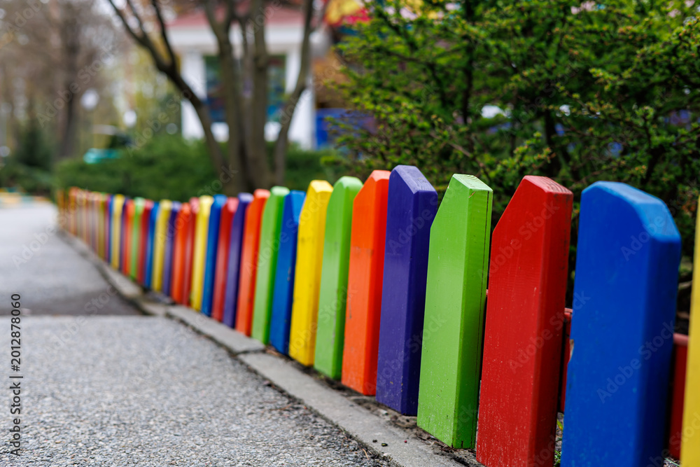 Fototapeta premium Bright multicolored wooden picket fence on a playground in a park, selective focus.