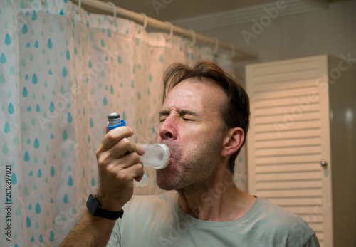Obraz na plátně Man using asthma inhaler with spacer for respiratory relief
