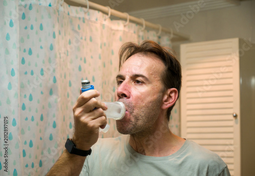 Obraz na plátně Man using asthma inhaler with spacer for respiratory relief