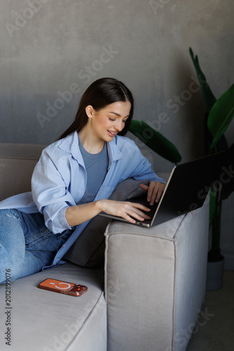Young woman using her laptop while relaxing on a sofa in a bright living room comfortable home