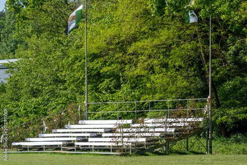 Canvas-taulu Outdoor bleacher seating near a sports field surrounded by green trees during da