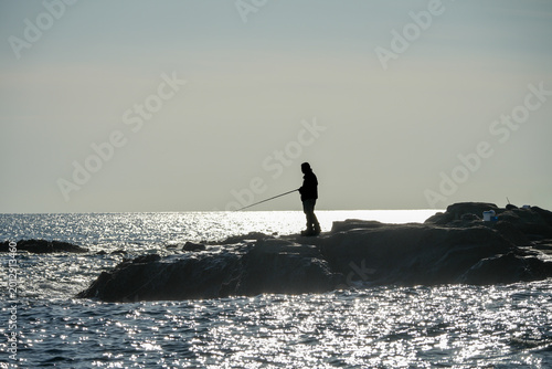 岩場の釣り人シルエット｜海辺レジャーに使いやすい背景写真