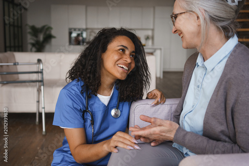 Senior woman and nurse sitting on sofa and talking at home, healthcare support, friendly communication, caregiver assistance, elderly care, trust, comfort living and home care concept