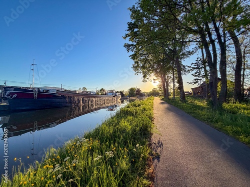 Bild auf Leinwand Peaceful canal towpath at sunset in Rijkevorsel, België with moored barge and wa