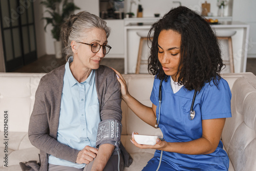 Fotografija Senior woman having blood pressure measured by nurse at home, healthcare monitor