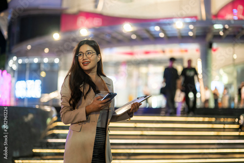 Businesswoman holding smartphone and clipboard at night in urban setting