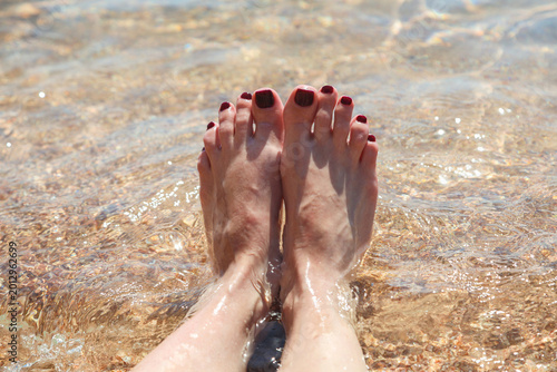 Women's feet with painted nails the sand in clear sea water.