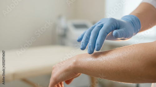 Dermatologist wearing blue glove examining skin on arm in clinic with soft light creating calm atmosphere for skin care and health checkup