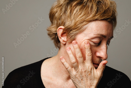 Schilderij op canvas Mature woman touching skin with thoughtful expression in natural aging and skincare concept
