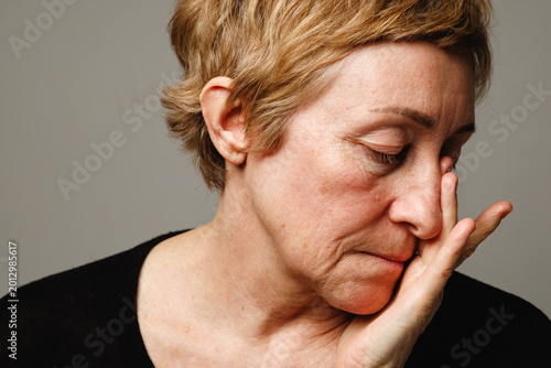 Portrait of mature woman with hand on face showing realistic skin and aging signs.