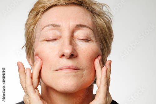 Portrait of senior woman touching face with natural skin texture and calm expression.