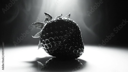 Dramatic monochromatic studio shot of a perfectly lit single strawberry with wispy smoke and reflection in a close-up