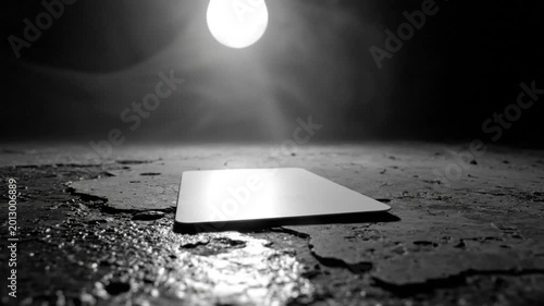 Dramatic black and white scene of a blank white card illuminated by a bright overhead light with a dark, textured background