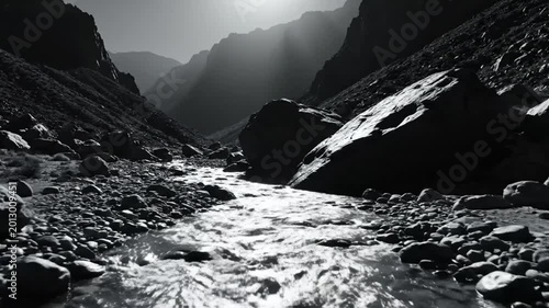 Black and white view of a sunlit river flowing through a rocky mountain canyon wilderness