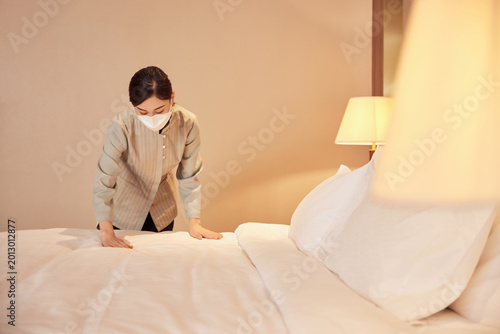 Obraz na plátně Masked hotel housekeeper making bed in guest room