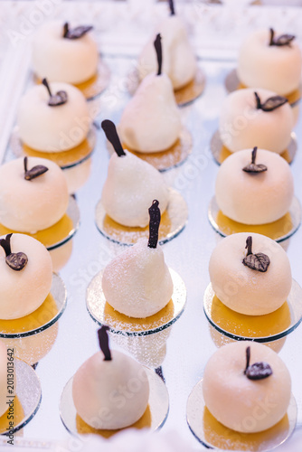 Fotografia Elegant white petit fours and pear-shaped desserts arranged on a mirrored tray f