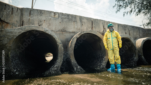 Environmental Worker Wearing Hazardous Protective Suit Standing Near Polluted Wastewater Drainage Tunnels During Industrial Contamination Inspection In Coastal Pollution Area