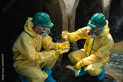 Environmental Workers Performing Chemical Wastewater Testing During Coastal Pollution Investigation While Wearing Hazardous Protective Equipment