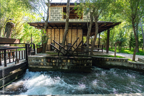 Powerful energy of flowing river turns traditional wooden water wheel at ancient Konigil Meros paper factory in Samarkand. Strong stream creates foam and motion in sunny day.