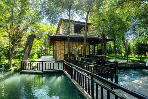 Traditional water wheel turning in river at ancient paper factory Konigil Meros near Samarkand. Sunny day, green trees, stone base and flowing water.