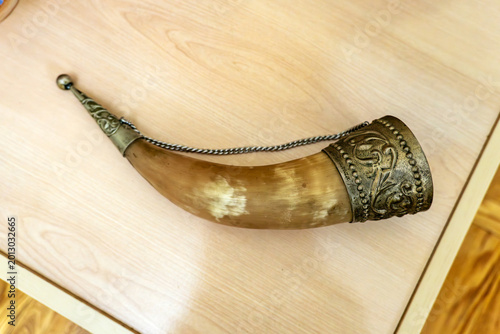 Drinking horn for wine on a table. Animal horn cup. Ancient Central Asian drinking vessel. Wooden stand. Tabletop still life.